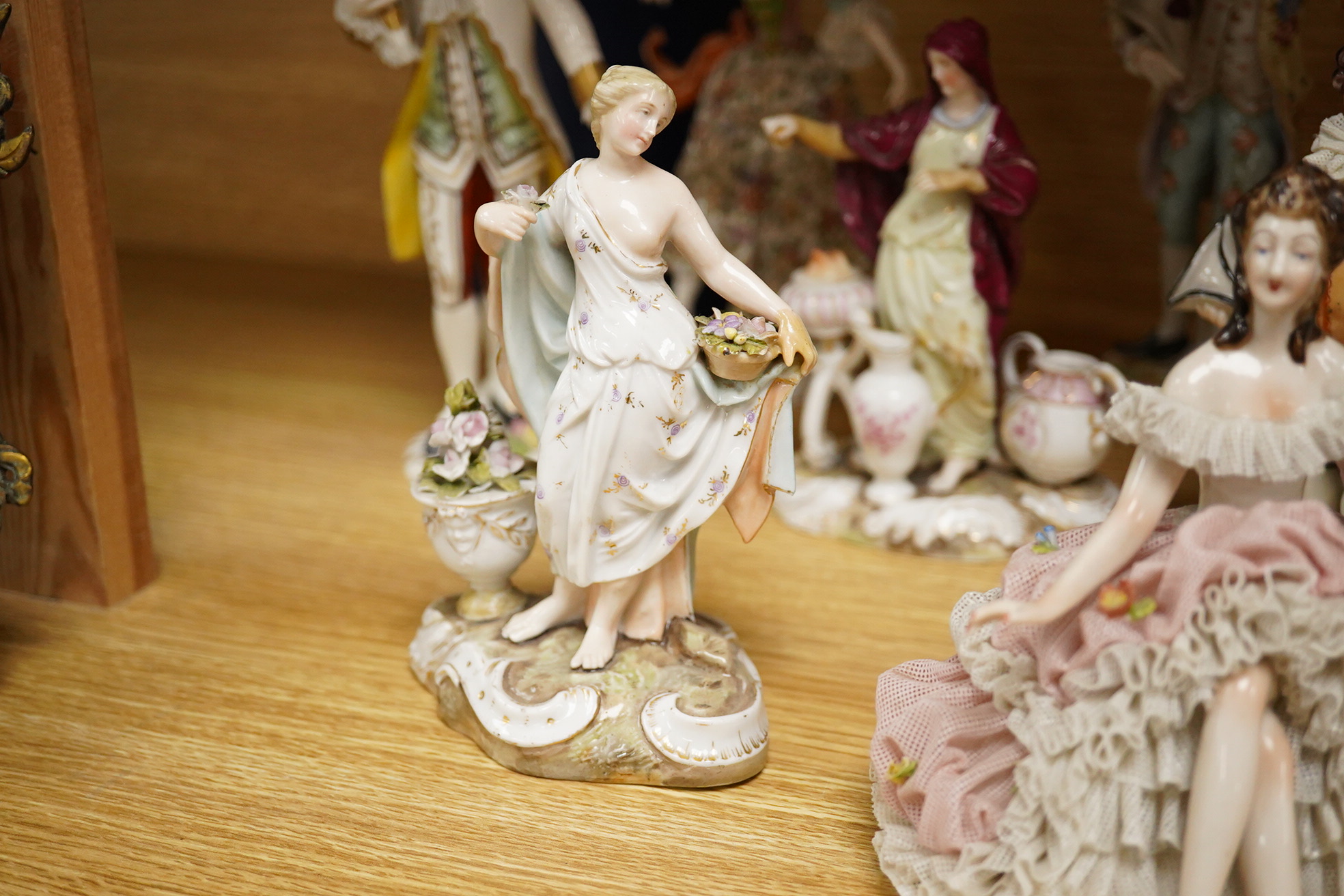 Nine continental figurines, to include Dresden porcelain lace examples, together with a resin figurine of Queen Elizabeth, largest 23cm high